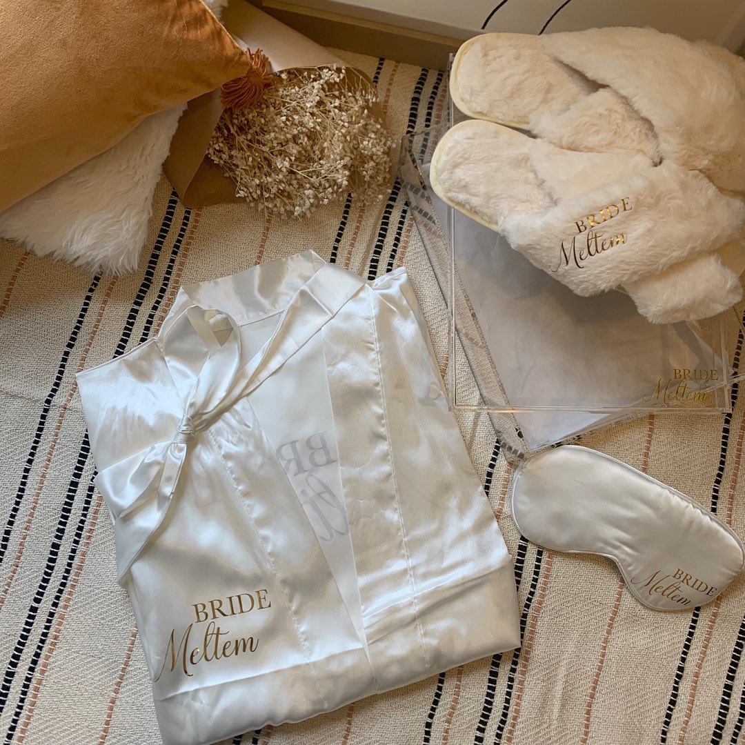 Coffret Bride Box personnalisé comprenant un pyjama en satin blanc, des chaussons fluffy et un masque de nuit avec broderie dorée pour mariée.